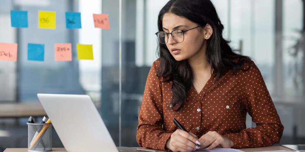 a woman at a laptop with documents before her concentrates on her screen.